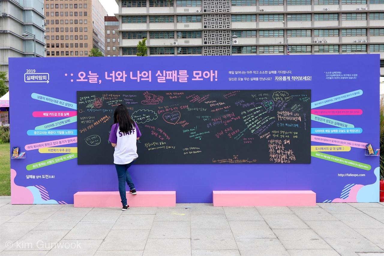 실패박람회의 게시판에 시민들이 실패에 대한 글을 적고 있다. 