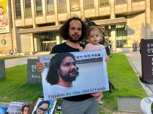  무삽 씨가 딸과 함께 이집트 정권에 비판적인 블로거 알라 압델 파타의 석방을 요구하는 사진을 들고 있다