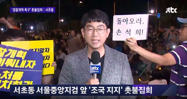 28일 JTBC <뉴스룸> 톱뉴스 <서초동 대규모 촛불집회…참가자들 "검찰 개혁" 촉구> 중 한 장면. 시위 참가자들이 "진실보도"를 외치는 가운데 '돌아오라 손석희!'라는 손 팻말이 눈에 띈다. 
