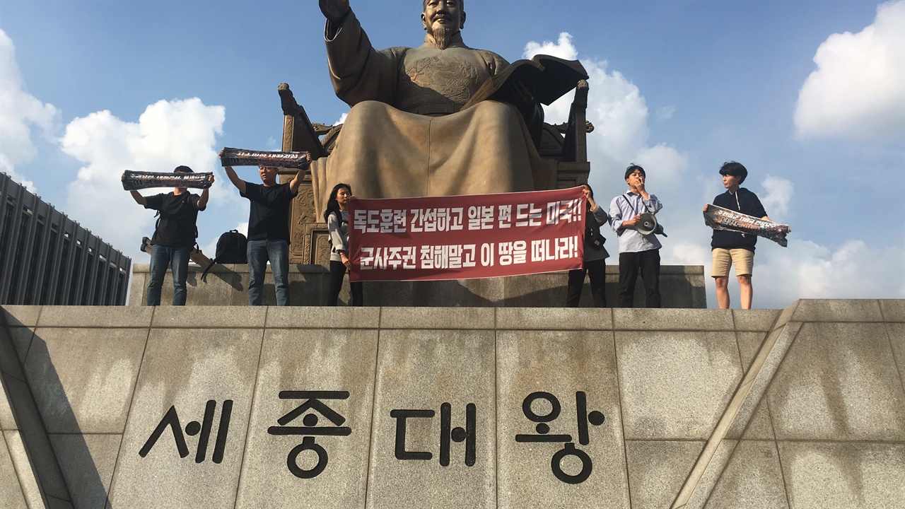 한국대학생진보연합 소속 대학생들이 세종대왕 상 위로 올라가 시위를 진행하고 있다