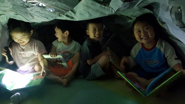 아산 월랑초병설유치원 유아들이 '책 놀이 축제' 기간 중 신문지 텐트 속에서 손전등을 비춰 책을 보는 책 텐트 놀이를 하고 있다.