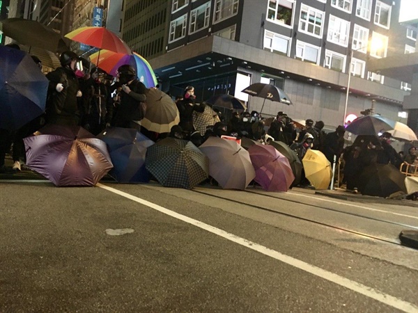 센트럴의 무장한 경찰에 맞서 검은 옷의 프론트 라인이 바리케이드로 저지선을 만들고 있다.