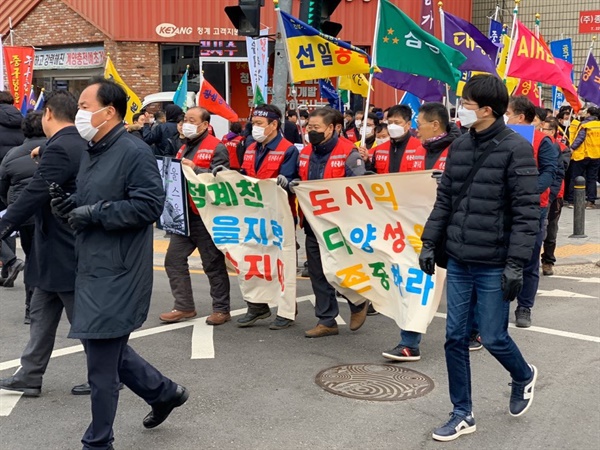 "도시의 다양성을 존중하라"라는 구호가 새겨진 현수막을 들고 행진하는 상공인과 시민들.