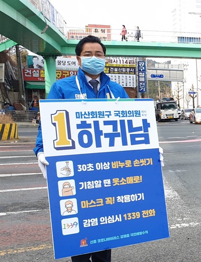 더불어민주당 하귀남 예비후보(마산회원)가 코로나19 예방수칙을 담은 손팻말을 들고 서 있다.