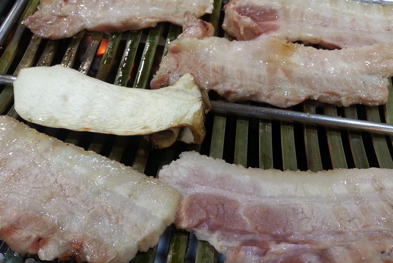 대나무 불판에서 서서히 익어가고 있는 돼지고기 삼겹살. 부드럽고 촉촉하게 보인다.
