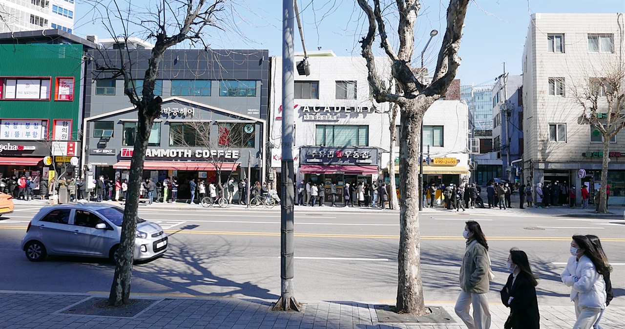 마스크를 쓰고 거리를 지나는 시민들 뒤편으로 마스크를 사기 위한 줄이 길다. 서울 성수동에 마스크를 통해 우리는 각자 어떤 이야기를 해야하는가? 언론은, 정책디렉터는 어떤 의제를 떠올리고, 방향을 잡아야 하는가. 