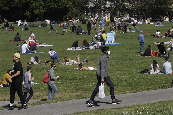 미국 캘리포니아 주 샌프란시스코의 한 공원에서 3일(현지시간) 코로나19 사태 속 휴식을 취하는 시민들 옆으로 마스크를 쓴 남성이 지나고 있다.
