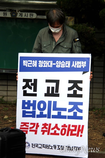 전국교직원노동조합 경남지부 조합원이 창원지방법원 앞에서 손팻말을 들고 서 있다.