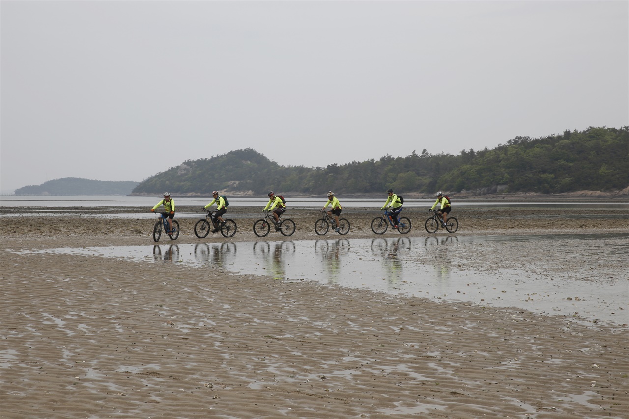 섬의 해변에서 자전거를 타며 여행을 하고 있는 동호인들. 바닷물에 비치는 두 바퀴가 환상경을 연출하고 있다. 바닷물이 빠진 신안 기점소악도의 진섬과 딴섬 사이 풍경이다.