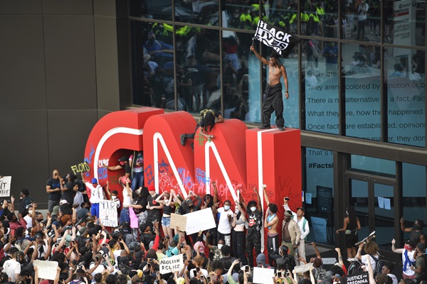 5월 29일(현지시간) 미국 조지아주 애틀랜타의 CNN 본사 앞에서 흑인 남성 조지 플로이드가 경찰의 가혹 행위로 숨진 사건에 항의하는 시위가 벌어진 가운데 한 시위 참가자가 'CNN' 로고 조형물 위에 올라가 '흑인의 생명도 중요하다'(Black lives matter)고 쓰인 깃발을 흔들고 있다.
