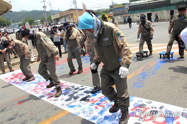 전국금속노동조합 경남지부가 6월 1일 창원진해 stx조선해양 앞에서 연 "stx조선해양 합의 불이행에 따른 지회 입장 발표와 결의대회". 노동자들이 발에 잉크를 발라 '산업은행, 무급휴직, 구조조정"이라 적힌 펼침막을 밟으며 지나가고 있다.