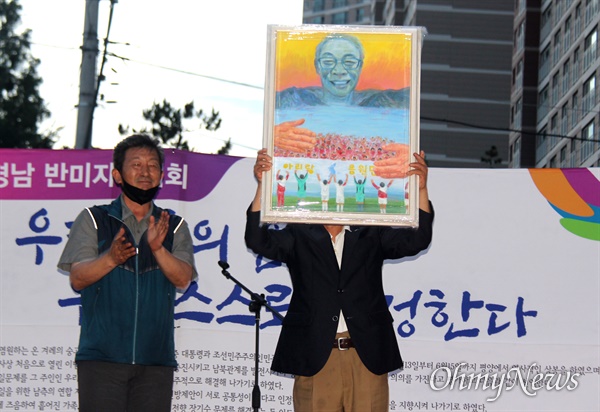 6.15경남본부는 6월 15일 저녁 창원 정우상가 앞에서 "6.15공동선언 20주년 기념식, 경남 반미자주대회"를 열었다. 김영만 고문이 신미란 작가가 그린 그림을 선물로 받은 뒤 들어 보이고 있다.