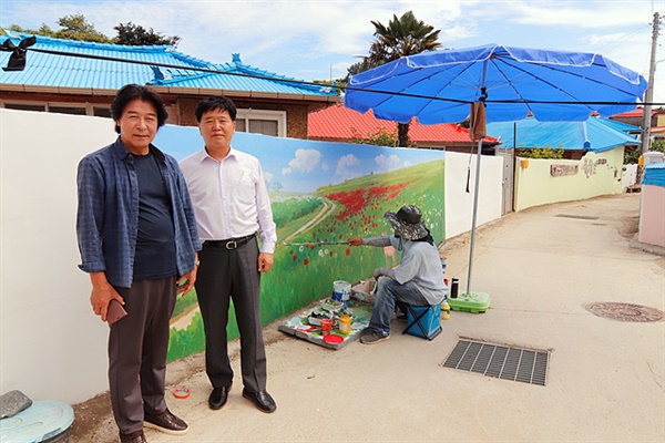 연홍미술관 선호남(왼쪽)관장이 작가의 담장벽화작업을 독려하고 있는 현장을 장세선(오른쪽)씨가 둘러보고 있다. 금산면 농협조합장과 고흥군의회 의장을 지냈던 장세선씨는 연홍도에 친척이 많이 살고 있다. 할머니형제, 고모, 이모, 누나까지 이 섬으로 시집왔다.  