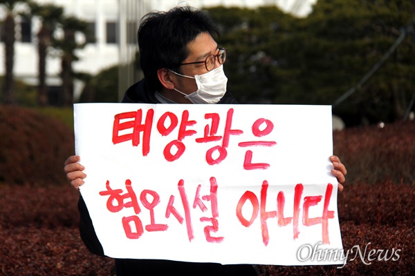 락 기후솔루션 이사가 12월 14일 경남도청 정문 앞에서 "태양광은 혐오시설 아니다"고 쓴 손팻말을 들고 서 있다.