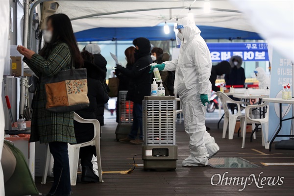  18일 오후 서울 성북구청앞에 설치된 코로나19 임시 선별진료소에서 시민들이 검체채취를 하는 동안 방호복을 입은 관계자들이 분무기 소독을 하고 있다.