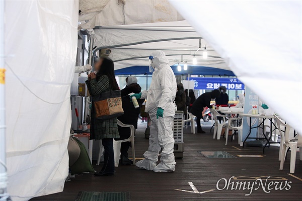18일 오후 서울 성북구청앞에 설치된 코로나19 임시 선별진료소에서 시민들이 검체채취를 하는 동안 방호복을 입은 관계자들이 분무기 소독을 하고 있다.