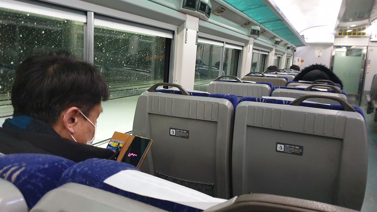 열차의 객실 내부. 승객들이 휴대전화를 검색하거나 잠을 자고 있다.