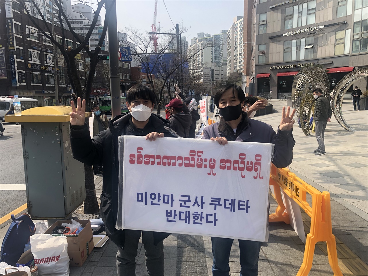  2021.3.7일 옥수동 시위현장 왼쪽 소모뚜와 오른쪽 개성문화원 민승준 조직위원장이  미얀마 군부 쿠테타 반대 집회에서 군사쿠테타 극복을 위해 세 손가락 사인을 내보이며 시위를 하고 있다. 