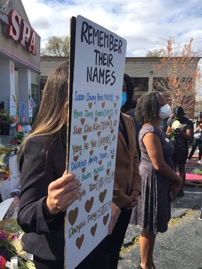 귀넷카운티 교육청 카렌 왓킨스 교육위원이 희생자 8명의 이름이 적힌 한 참석자의 피켓을 빌려 들고 서 있다. 뒤쪽에는 "엿먹어라! '나쁜 날', 페티쉬, 고정관념, 인종차별, 여성혐오!"가 써 있다.