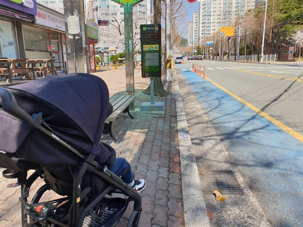  아이가 탄 유모차가 버스정류장에 서 있다. 