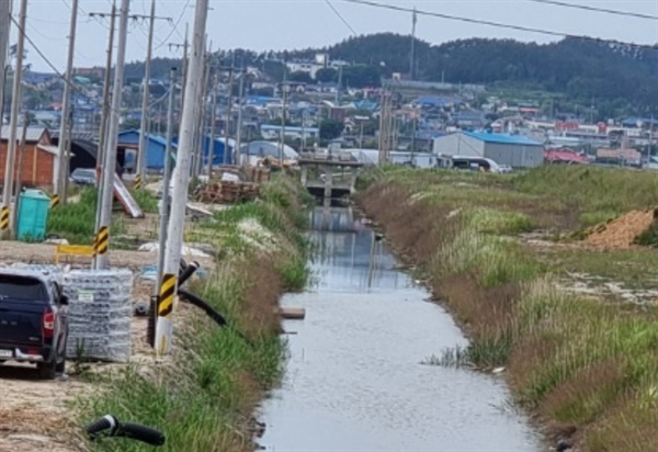 굳게 닫힌 수문 사진은 문제의 배수로로 사진 오른쪽이 염수를 바다로 빼 내는 모터가 설치된 건물이고 배수로를 따라 위쪽에는 수문이 보인다. 농민들은 이 수문을 개방하고 모터를 상시 가동해 염전과 양어장에서 나오는 염수를 바다로 빼내야 염해 피해가 발생하지 않는다고 주장하고 있다.
