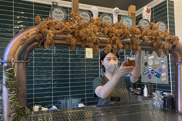 김예지 대표가 탭에서 맥주를 따르고 있다. 탭 위쪽에는 다양한 형태의 핸들이 달려 있다. 탑을 감고 있는 것은 마른 홉이다.