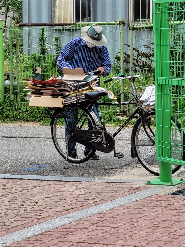 어르신 한 분이 자전거를 타고 와서 도시락을 받아 자전거 뒷자리에 가득 실린 박스 위에 올리고 떨어지지 않도록 잘 고정시키고 계십니다.