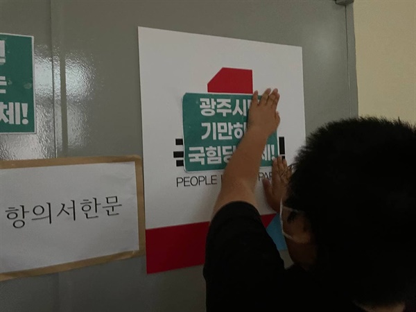 한 기자회견 참가 대학생이 당사 사무실 문 앞에 국민의힘을 규탄하는 손피켓을 부착하고 있다.