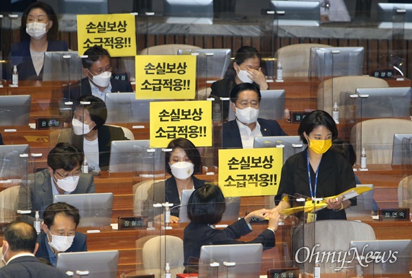 정의당 류호정 의원이 1일 오후 국회 본회의에서 '손실보상 소급적용'이라고 적힌 손팻말을 나눠주고 있다.