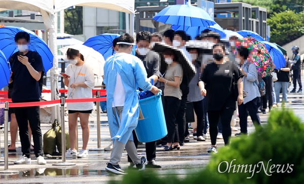 전국적으로 폭염특보가 내려진 22일 서울 중구 서울역 광장에 마련된 코로나19 선별진료소에서 검사 대기시간이 길어지자, 방역요원이 햇볕을 피할 수 있도록 시민들에게 우산을 나눠주고 있다.
