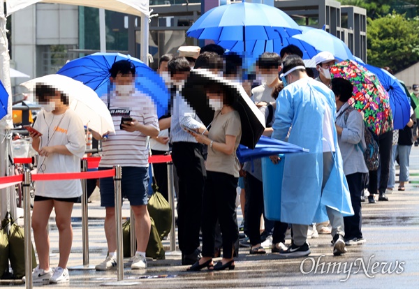 전국적으로 폭염특보가 내려진 지난 22일 서울 중구 서울역 광장에 마련된 코로나19 선별진료소에서 검사 대기시간이 길어지자, 방역요원이 햇볕을 피할 수 있도록 시민들에게 우산을 나눠주고 있다.
