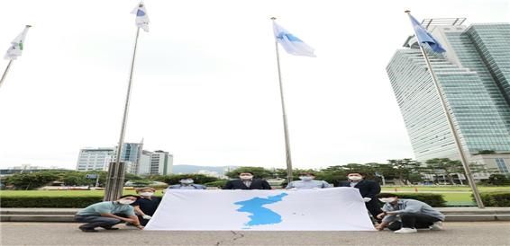 8월 3일 안양시청에서 최대호 시장이 3개 평화통일단체의 대표들과 함께 태극기가 걸려있는 바로 옆에 한반도기를 게양하고 기념사진을 찍고 있다.
