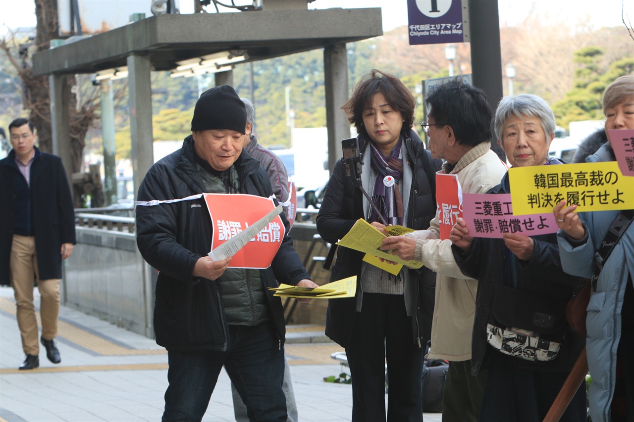 일본 시민단체 '나고야 미쓰비시 조선여자근로정신대 소송을 지원하는 모임' 한 회원이 '판결이행'이라고 적힌 어깨띠를 메고 시민들을 상대로 전단지를 배포하고 있다. 지난해 1월 17일 금요행동 500번째 모습