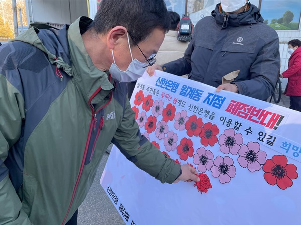 "꽃 피는 봄에도 신한은행을 이용할 수 있길 희망합니다"라고 적힌 피켓에 주민들이 꽃모양 스티커를 부착하고 있다.