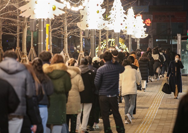  신종 코로나바이러스 감염증(코로나19) 신규 확진이 연일 7천 명대를 기록하는 등 방역 한계 상황에 다다르자 정부가 다시 사회적 거리두기 단계 강화를 발표한 16일 오후 서울 서대문구 신촌역 광장에 마련된 선별진료소를 찾은 시민들이 성탄과 연말을 상징하는 트리 조명 아래 코로나19 검사를 받기 위해 줄지어 서 있다. 