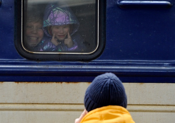 6일 우크라이나 키이우 중앙 기차역에서 열차에 탄 한 소녀가 가족인 듯한 남성을 향해 입꼬리를 올리라는 몸짓을 취하고 있다.