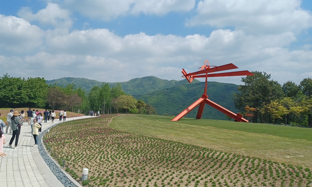 원주 뮤지엄산 입구 붉은 조형물과 산, 하늘, 꽃 등이 조화를 이루고 있다.