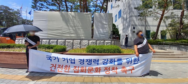 6월 7일 오전, 서울 서초구 양재동 현대기아차 본사 앞. 회사명이 써있는 비석 앞에 현대기아차가 고용한 것으로 추청되는 청년들이 '건전한 집회문화 정착 촉구' 현수막을 들고 서 있다. 