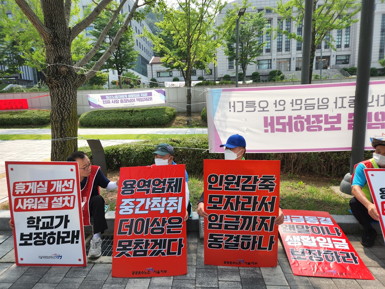 지난 7월 5일, 오전 시위에 나서기 전 연세대 청소노동자들이 플래카드를 들고 바닥에 앉아 있는 모습. 