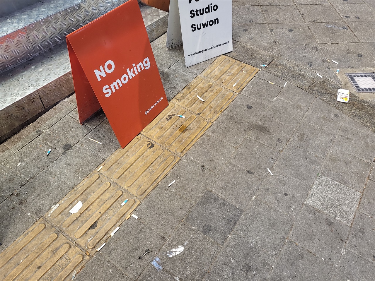 수원역의 한 가게 앞, ‘NO Smoking’이라는 문구가 새겨진 입간판 앞에 담배꽁초와 담뱃값이 버려져 있다. 