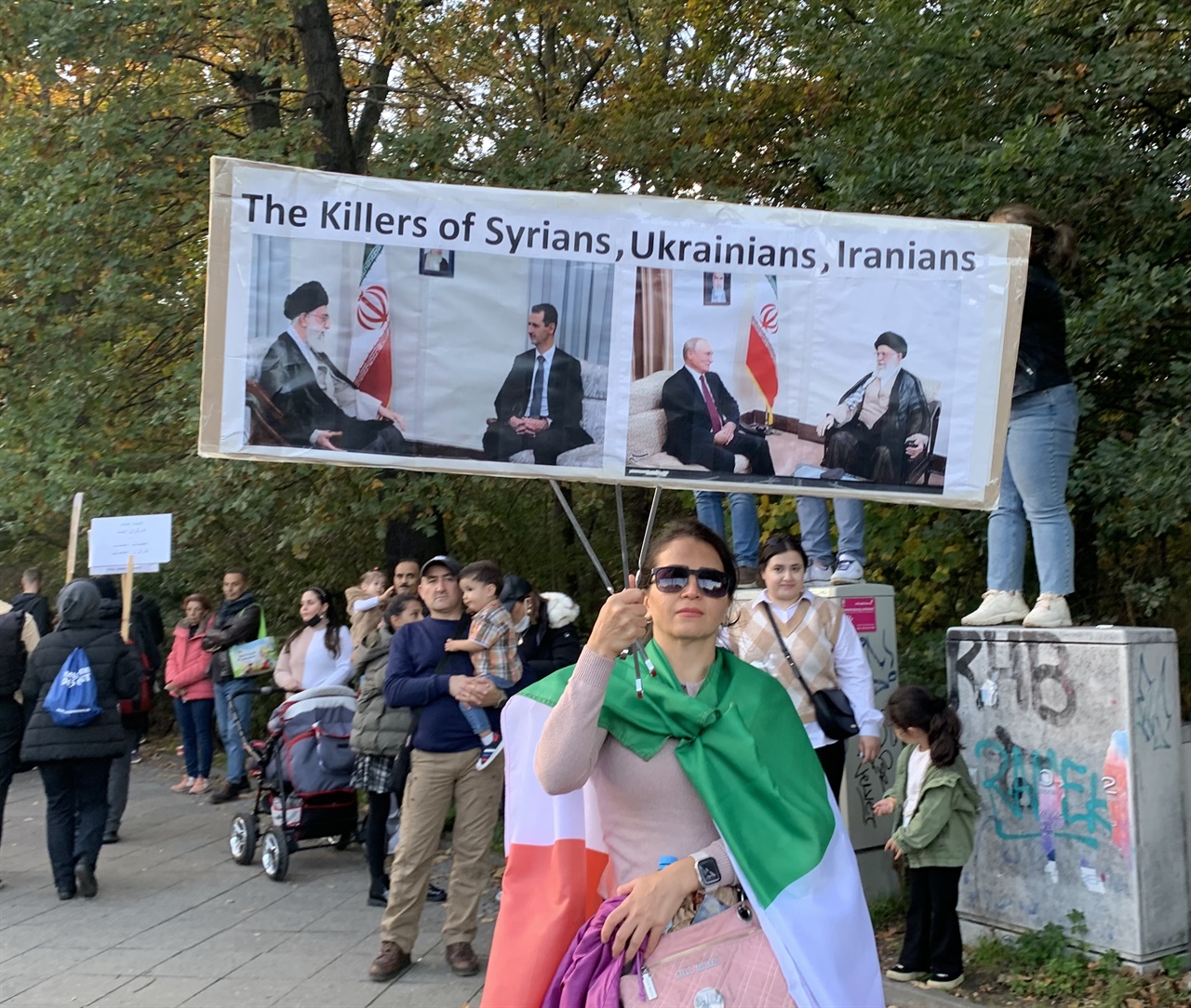 이란 정부의 시리아전쟁, 우크라이나 전쟁에의 관여를 비판하는 듯한 손팻말을 들고 있는 집회 참가자. "시리아인들, 우크라이나인들, 이란인들의 킬러"라고 씌였다.