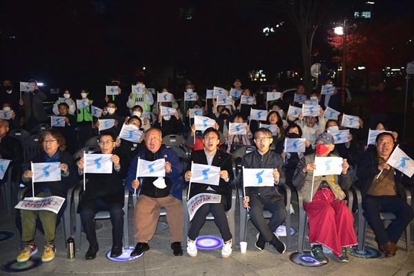 제5회 대전평화통일문화제가 11월 21일(월) 저녁 7시에 대전 평화의소녀상 앞에서 진행되었다. 참가자들이 ‘단일기’를 펼치고 구호를 외치고 있다.