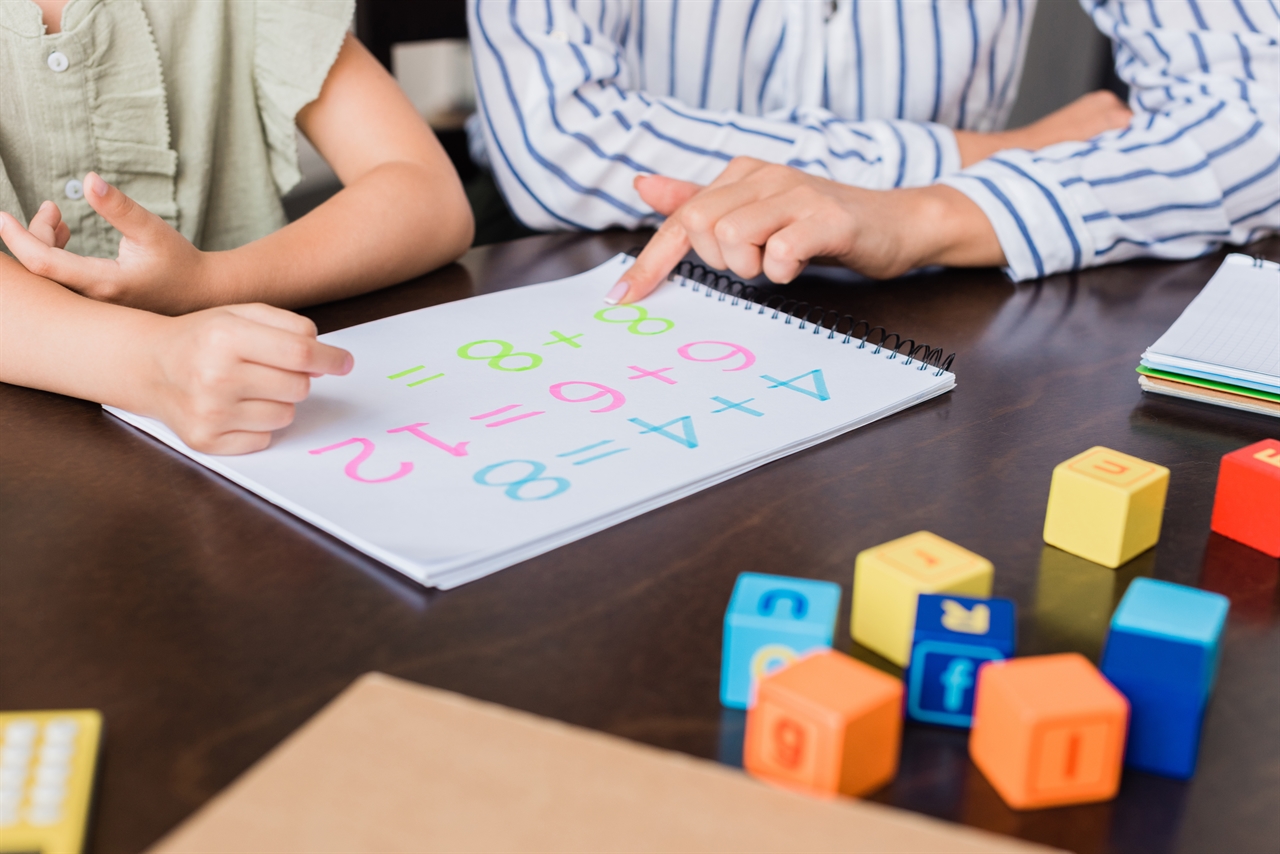 초등 저학년 아이들이 수학 문제집을 푸는 걸 도와주고 있다.