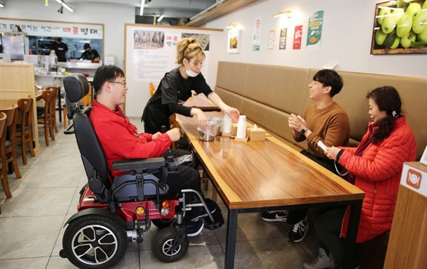 전동 휠체어를 탄 유청민 씨가 ‘모두의 가게’에서 동료들과 식사하며 보통의 일상을 즐기고 있다.