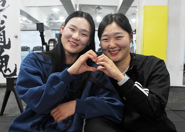  이수빈 선수와 김하영 선수가 다정하게 웃으며 손하트를 만들어 인사하고 있다. 