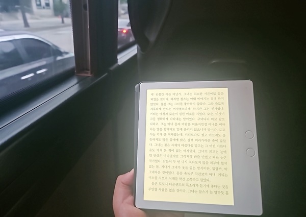 통근버스 안에서 이북리더기로 책을 읽는 여유를 갖다