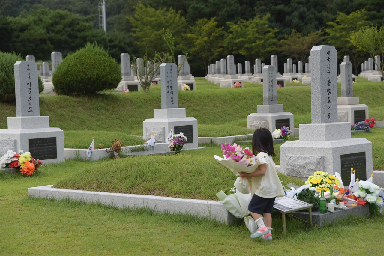  아이가 꽃다발을 홍범도 장군 묘 앞에 놓고 있다.