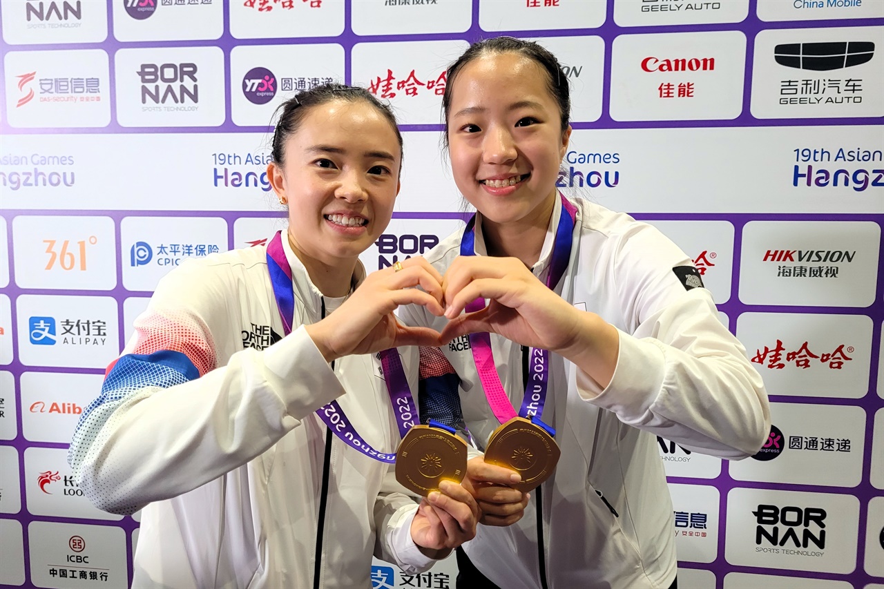  아시안게임 탁구 여자 복식에서 금메달을 따낸 신유빈(오른쪽)과 전지희(왼쪽) 선수가 금메달을 한 손에 들고, 다른 한 손으로 '하트'를 그려보이고 있다.