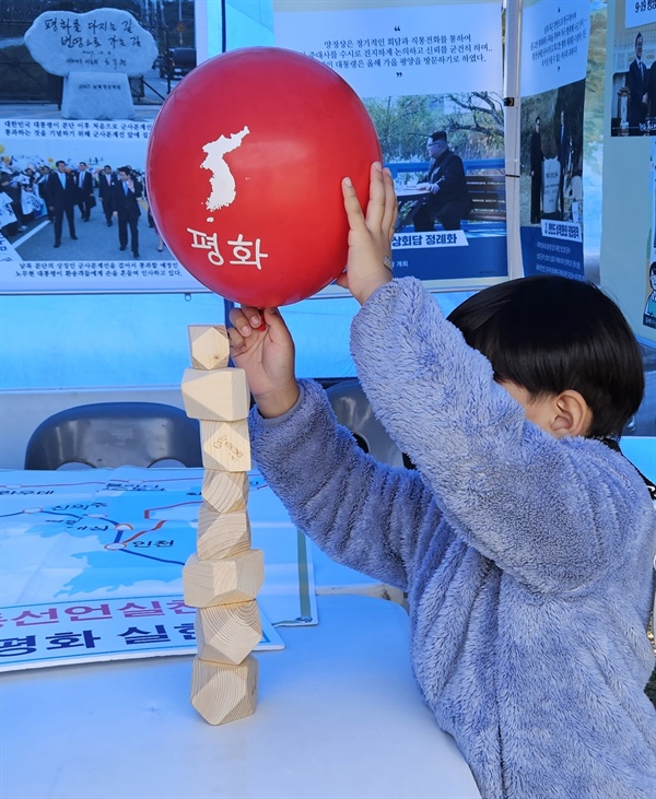 한 어린이가 통일염원 탑을 쌓고 '평화'라고 씌어 있는 풍선을 올려서 창의력을 발휘하고 있다.