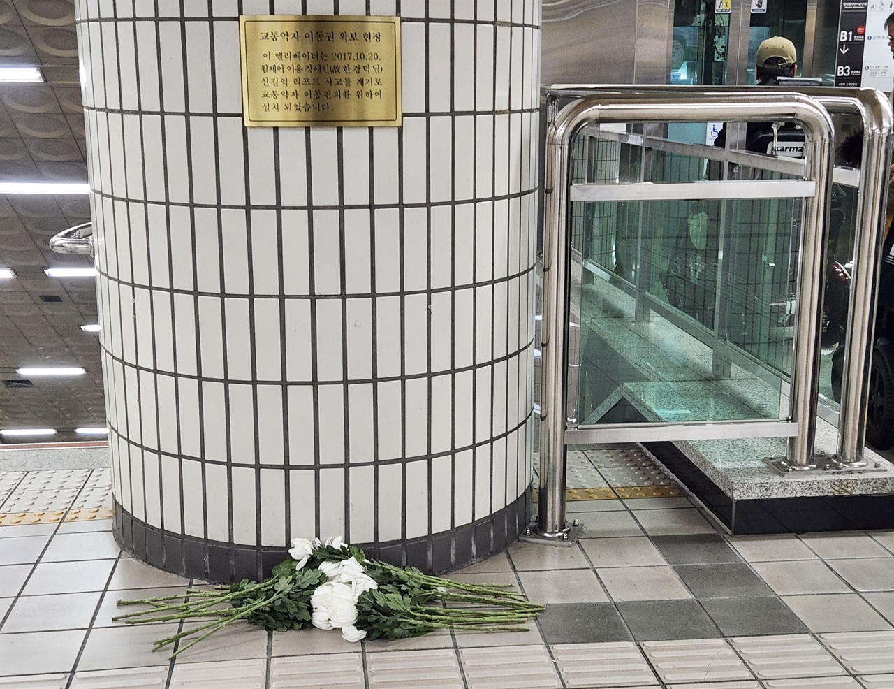 신길역 환승구간 엘리베이터 앞에 ‘교통약자 이동권 확보 현장’이라는 문구를 새긴 동판이 세워졌다. 동판 앞에 국화꽃들이 놓여 있다. 